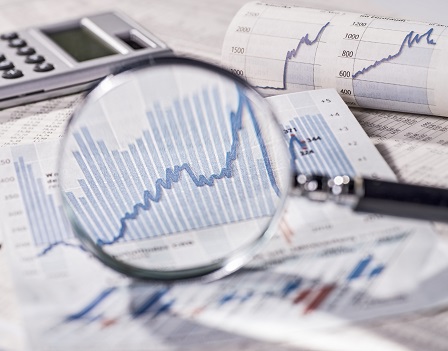 A magnifier shows the positive development of share prices. In the background, other curves with trading prices and a calculator can be seen.