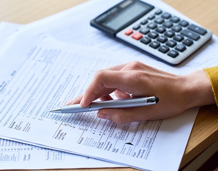 Close-up of unrecognizable woman working with tax return form: she checking papers and using calculator