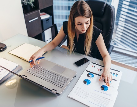 Female businesswoman readind financial report analyzing statistics pointing at pie chart working at her desk.